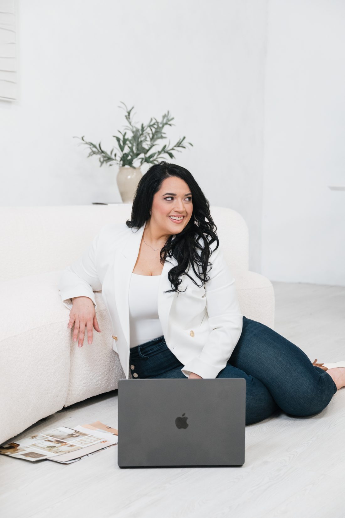 Yvette Ramos in a white blazer, sitting on a white sofa with her laptop.